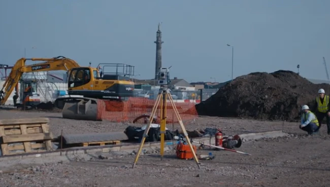 Two civil engineers using a theodolite to survey a construction plot, with an excavator working in the background, demonstrating the precision and teamwork in construction surveying.