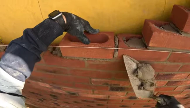 A skilled bricklayer placing a brick onto mortar with one hand, while holding a trowel with fresh mortar in the other hand, showcasing masonry craftsmanship.