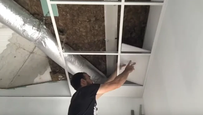 A ceiling fixer installing a custom-cut plasterboard into a precise gap in the ceiling, demonstrating skill and attention to detail in interior construction.
