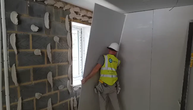 A young skilled dryliner holding a plasterboard, ready to install it, showcasing expertise in interior wall and ceiling construction.
